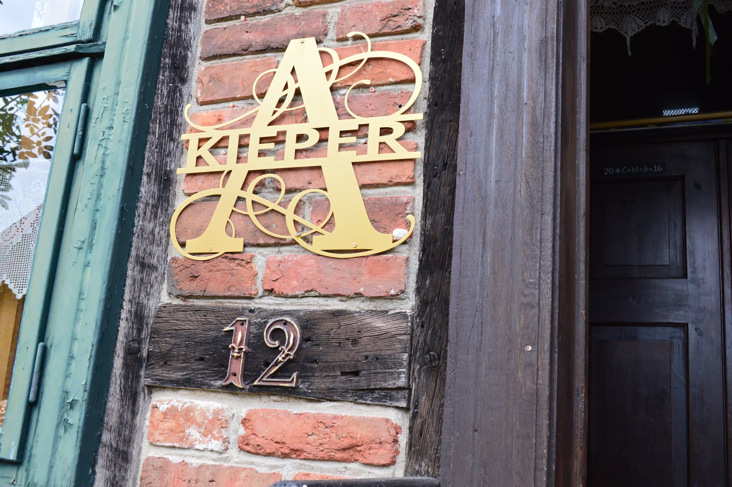Goldenes Monogramm „A. Kieper“ an der Backsteinwand des historischen Forsthauses, darunter die Hausnummer 12